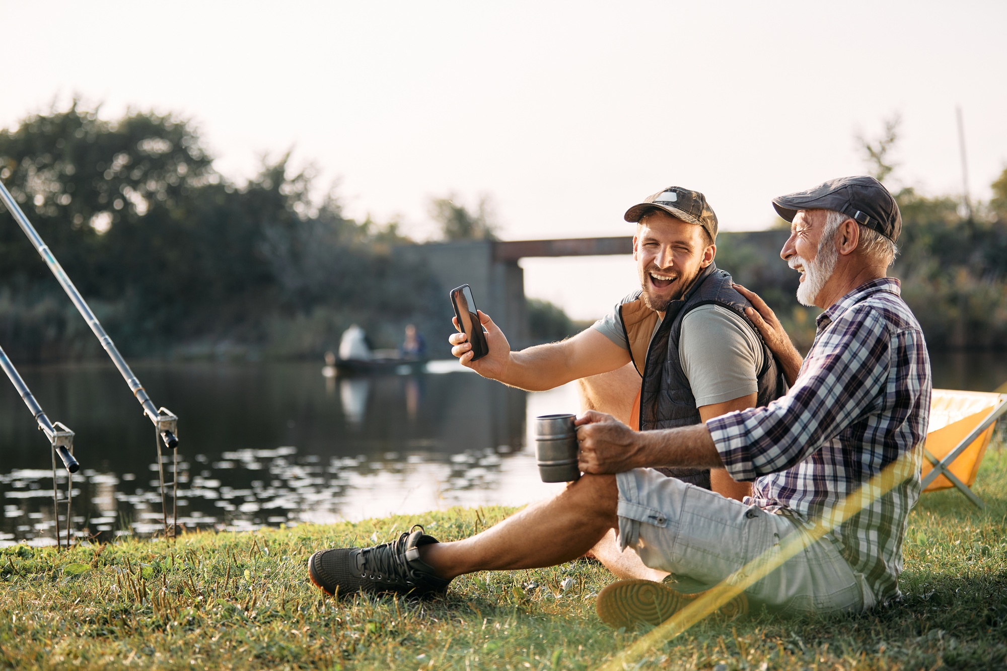 Cheerful father and son having fun and laughing while fishing by the river.