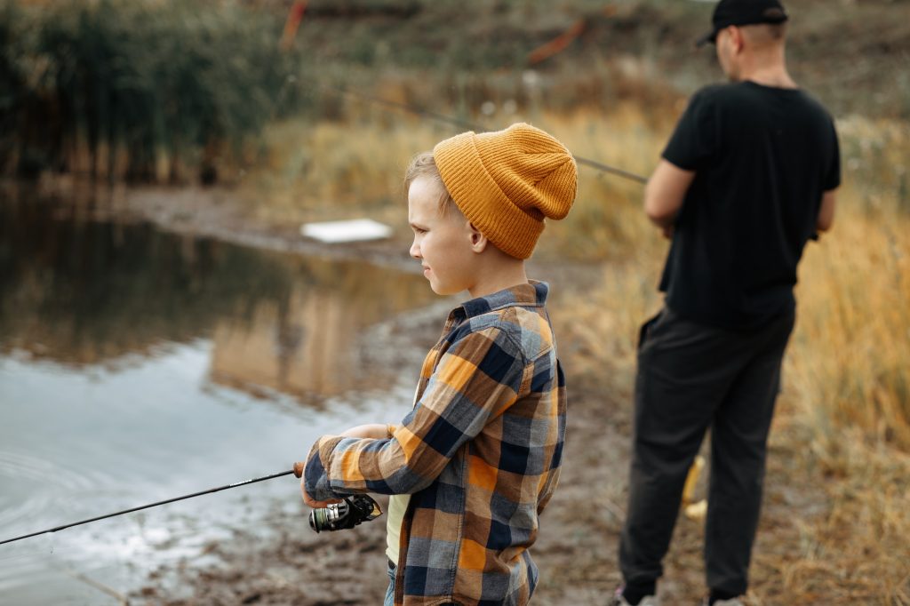 Kid teen boy catching a fish with dad in the lake, river or pond