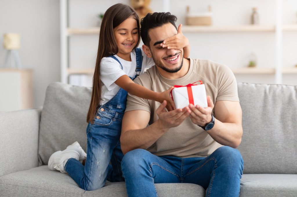 Little girl celebrating father's day, greeting excited dad with box