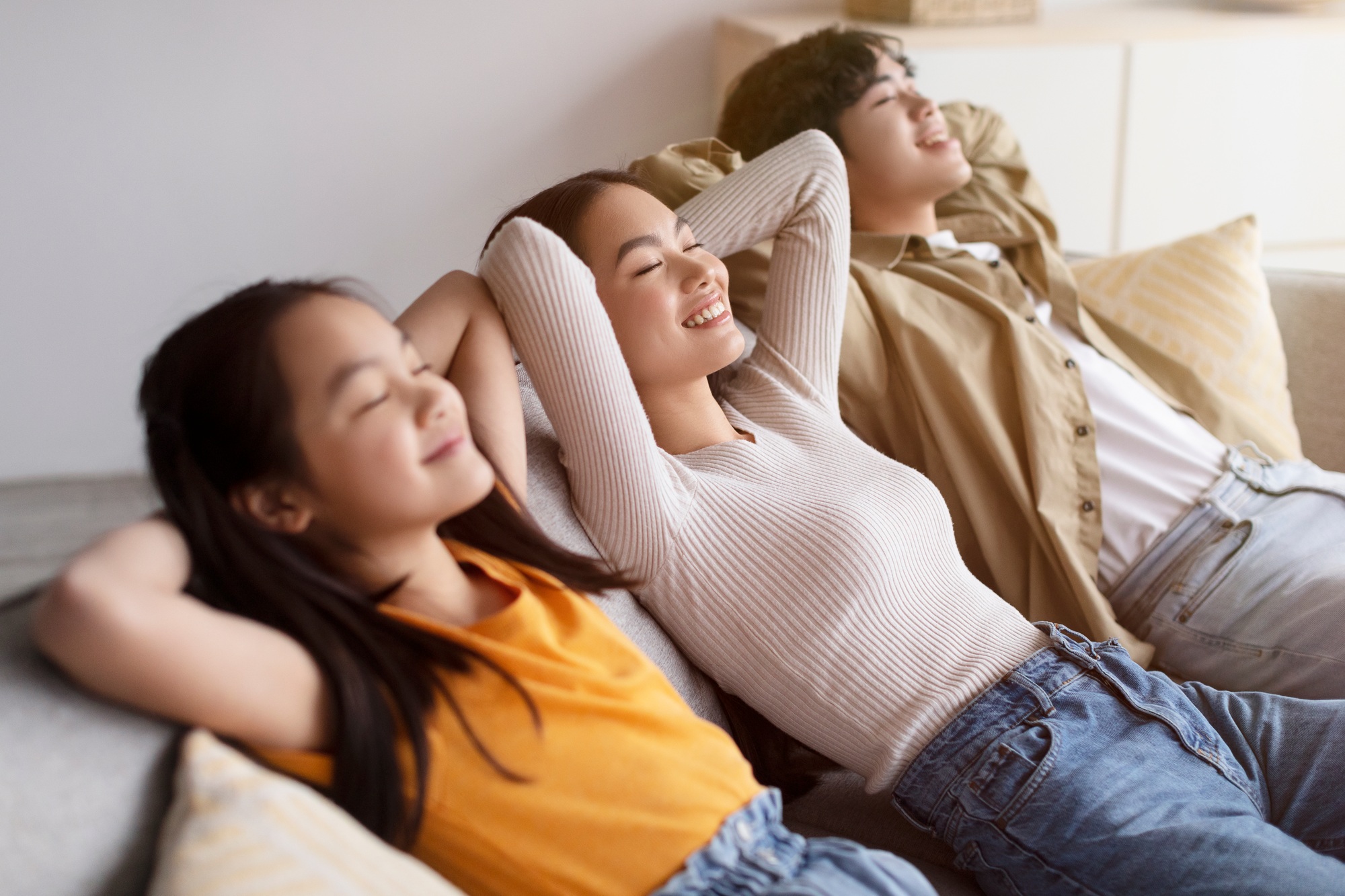 Smiling millennial asian couple and teen daughter relaxing on sofa with closed eyes